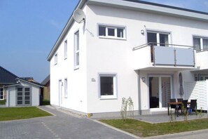 A two-story white house with a balcony, a satellite dish, and a small garden area. - Tacke 2 Comfortable holiday residence (Burg a. Fehmarn)
