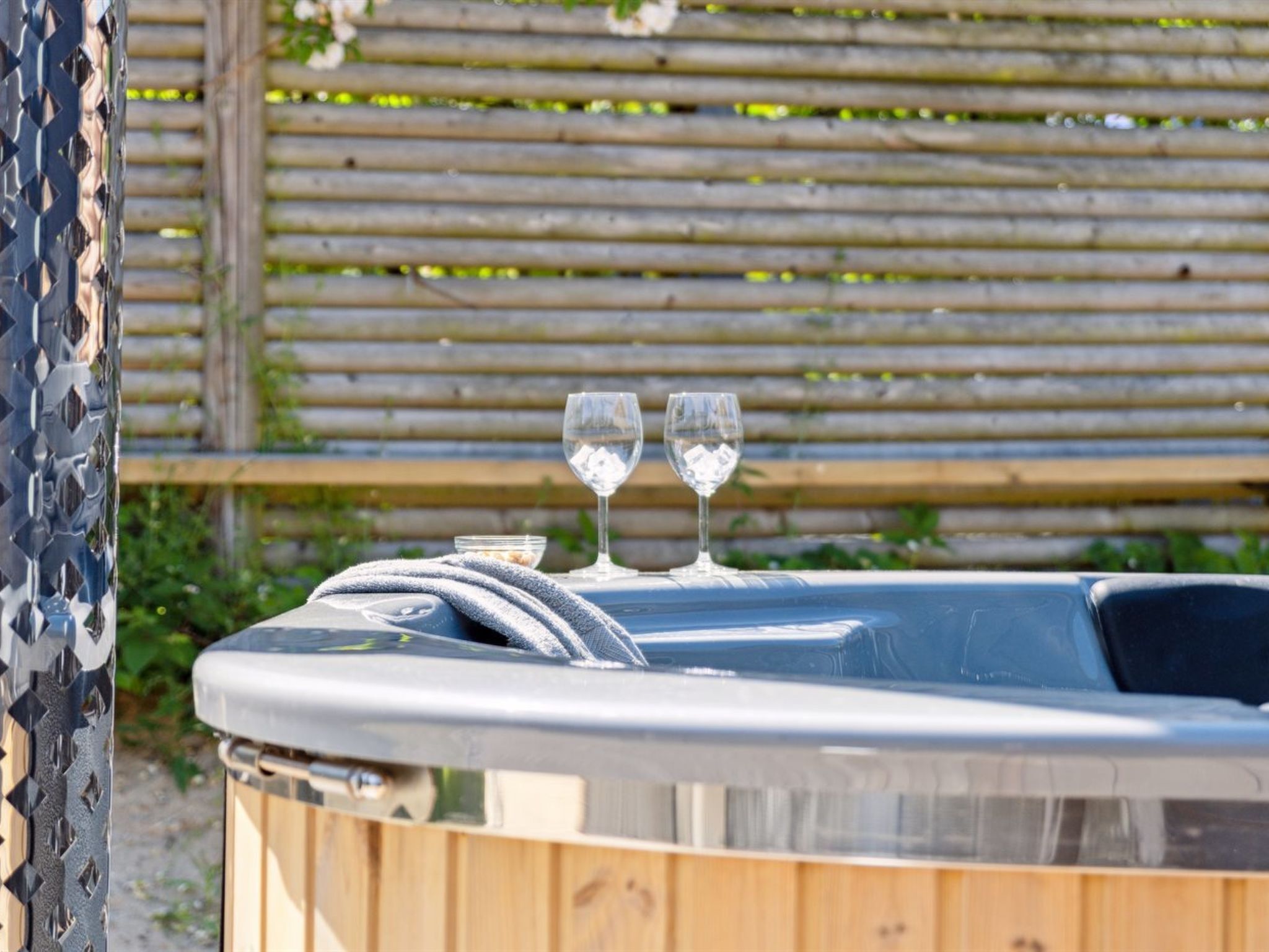 Een hottub met twee glazen water erop, omringd door een houten omheining.