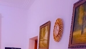 A room with a flat-screen TV mounted on the wall, a white table with decorative vases, and framed artwork. - Lux Suites Vee Studio Apartments Bamburi (Mombasa)