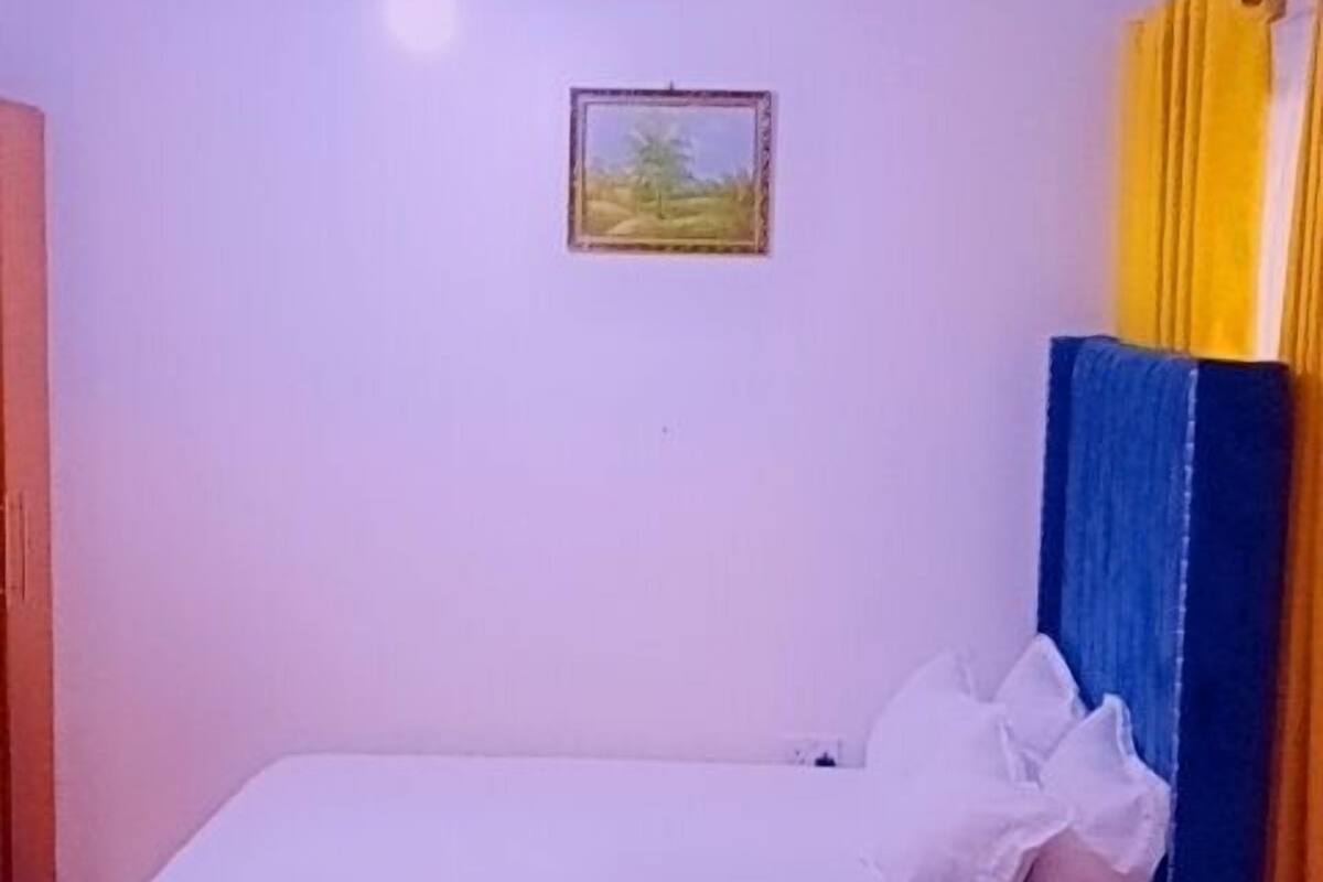 A small, cozy room with a bed, a blue sofa, a yellow ottoman, and a ceiling fan.