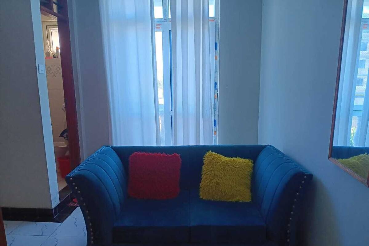 A blue sofa with red and yellow cushions in a room with a window and curtains.