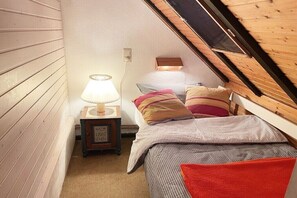 Une petite chambre mansardée, chaleureuse, avec un plafond en pente, un lit simple, une table de chevet avec une lampe et un tableau encadré.