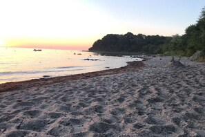 A beach with a sandy shore, a calm sea, and a forested hill in the background.