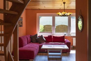 Een gezellige kamer met een houten wenteltrap, een rode hoekbank, een witte tafel en een raam met uitzicht op een bakstenen muur.