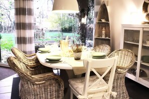Enjoy meals in this cozy dining area with a round table for four, surrounded by wicker chairs and a beautiful garden view.
