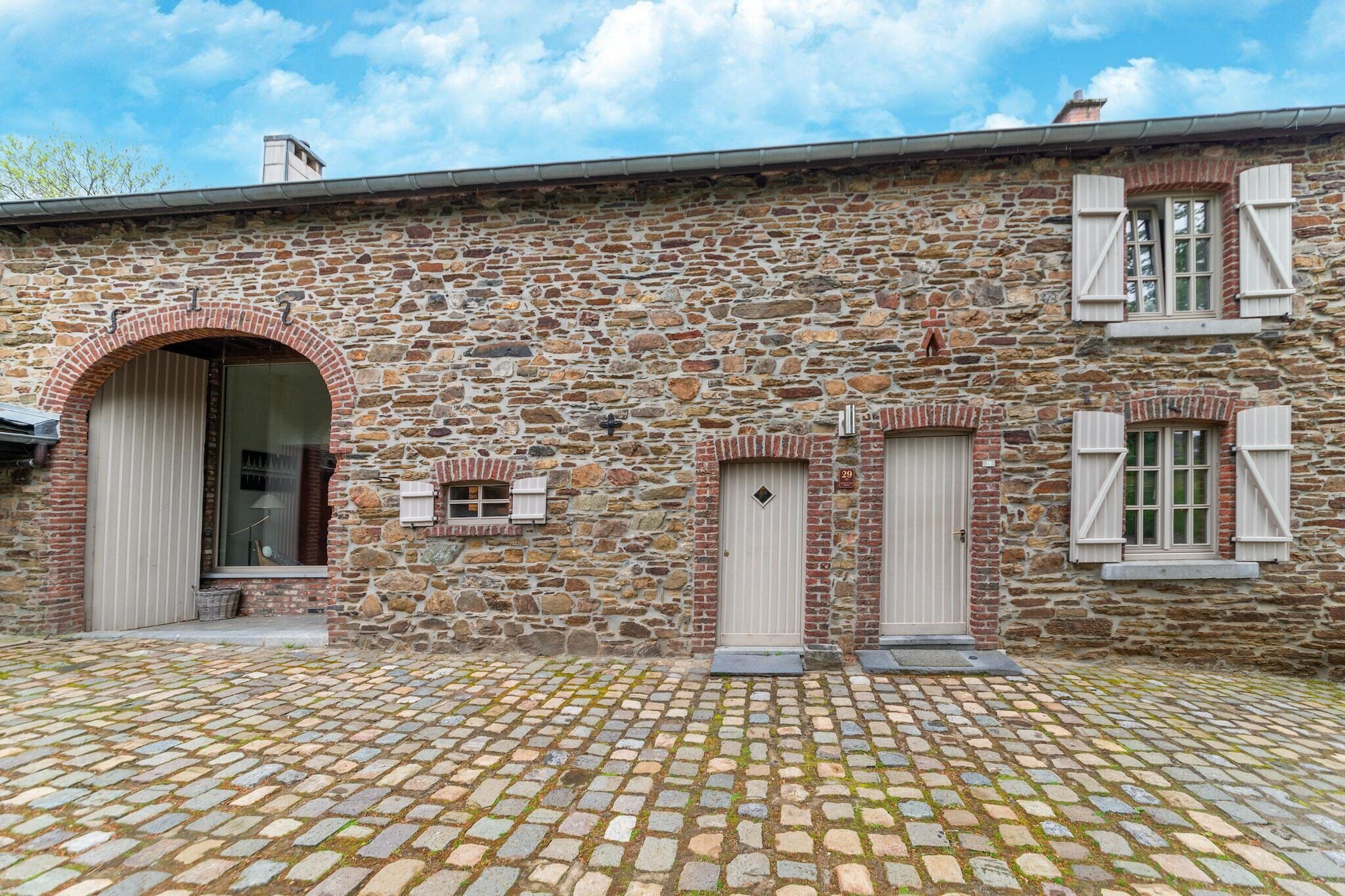 A stone building with a cobblestone courtyard, a large arched doorway, and two small windows with shutters.