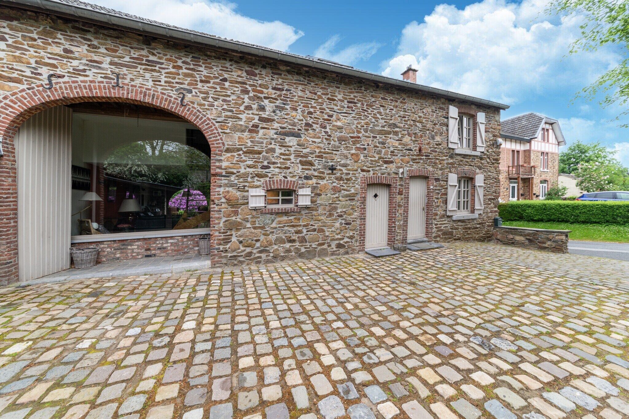 Un bâtiment en pierre avec une allée pavée, une grande entrée en arc de cercle et un petit jardin.