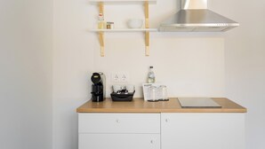 Una cucina con una macchina da caffè, un vassoio nero, una bottiglia d'acqua e un computer portatile sul piano di lavoro. Due pensili bianchi sotto.