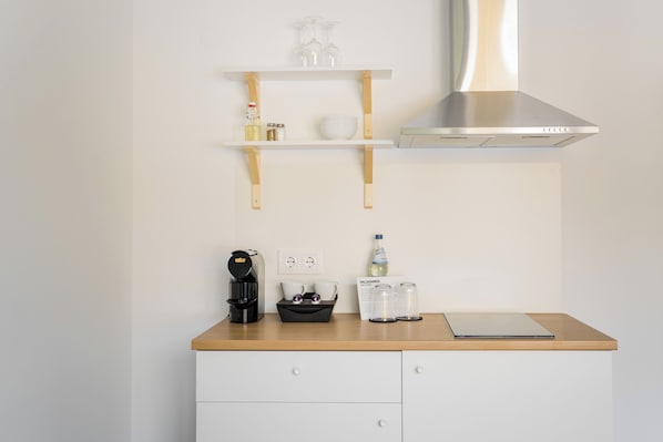 A kitchen with a coffee maker, a black tray, a water bottle, and a laptop on the counter. There are two white cabinets below.