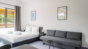 Una habitación de hotel moderna con una cama, un sofá gris, una mesita pequeña y dos cuadros en la pared.