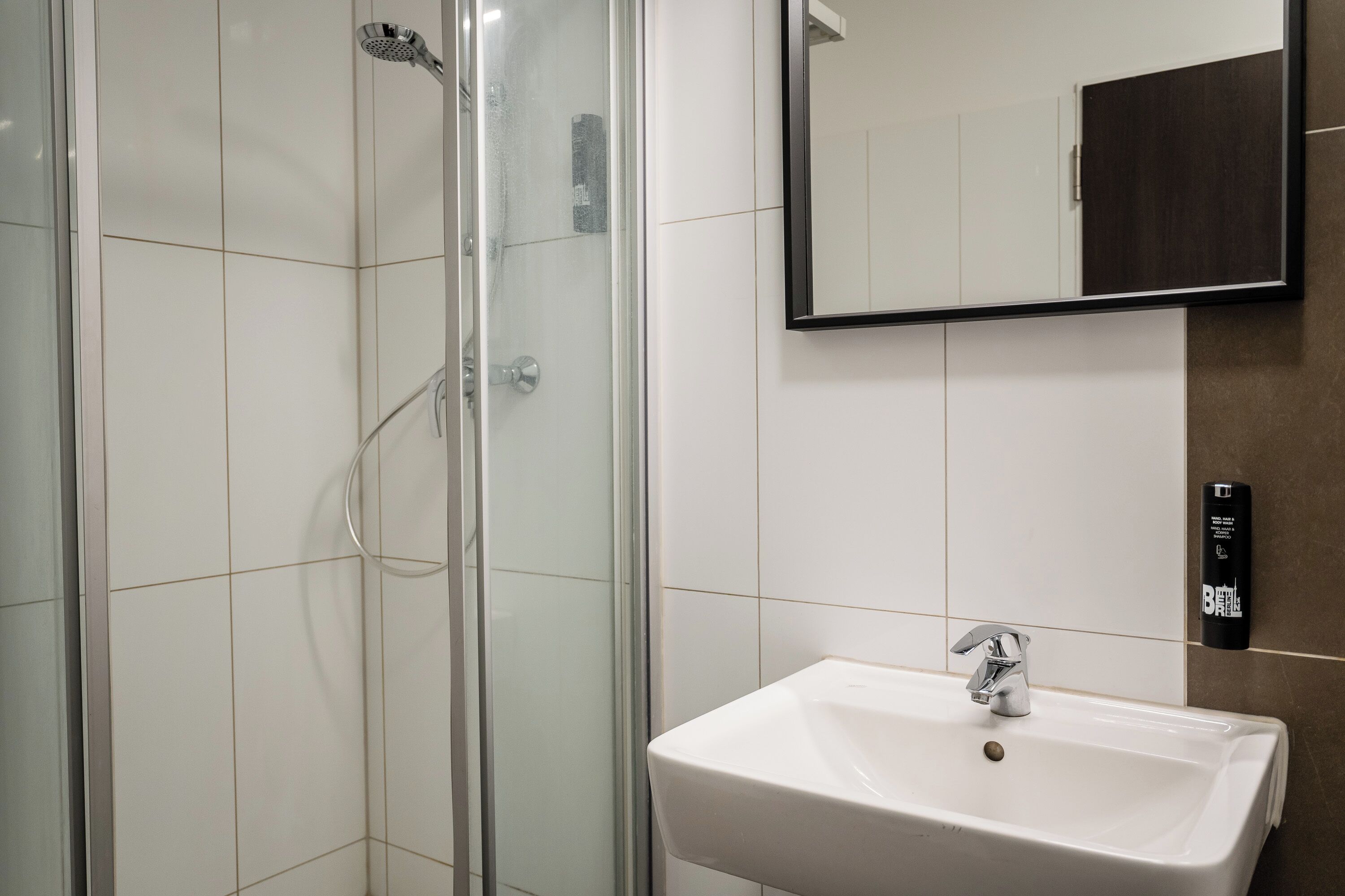 A modern bathroom with a glass shower enclosure, a white sink, and a mirror above it.