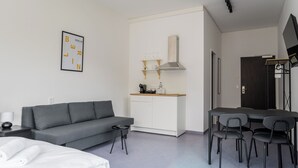 Una camera d'albergo moderna con un divano grigio, un piccolo tavolo da pranzo con sedie, un angolo cottura e un grande specchio.
