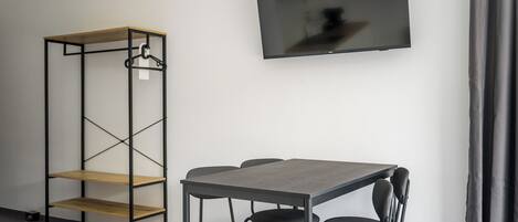 Et moderne værelse med en træreol, et gråt bord med fire stole og et fladskærms-tv ophængt på væggen.