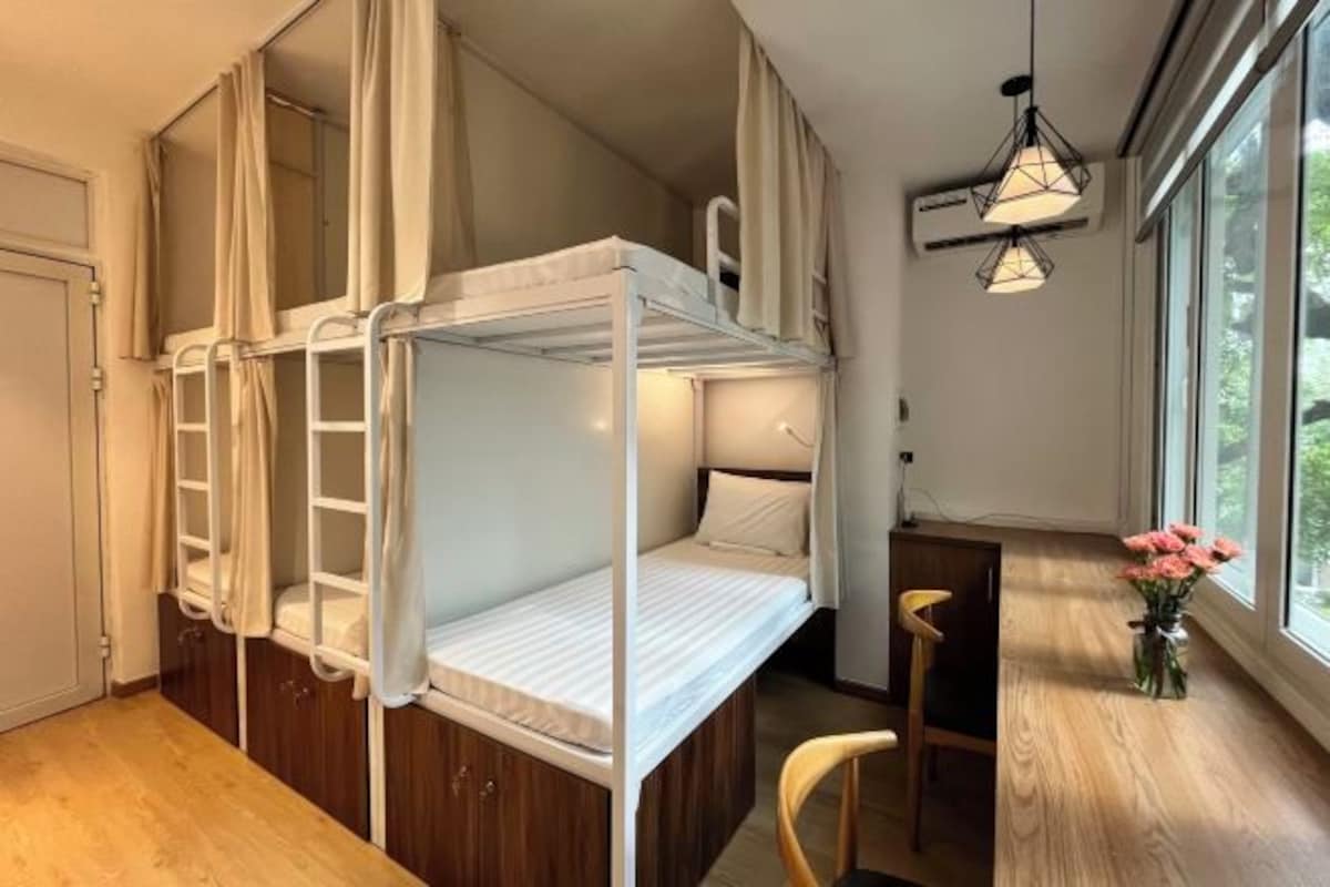 A room with bunk beds, a desk, a chair, and a window with curtains.
