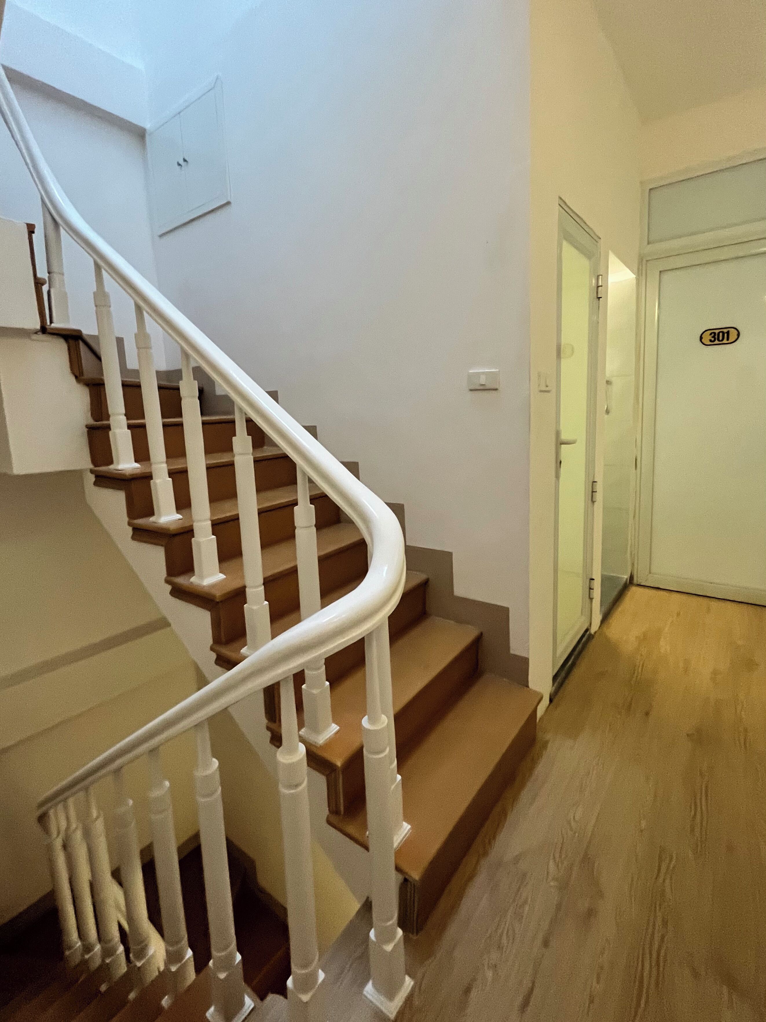 A staircase with white railings and wooden steps leading to a door marked with the number 301.