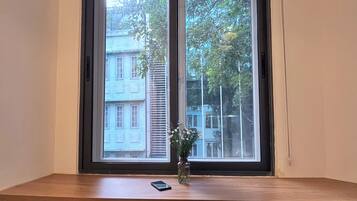 A room with a wooden table and two chairs, a window with blinds, and a vase with flowers on the table.