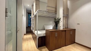 Habitación de hotel compacta con literas, un armario de madera y una pequeña zona de escritorio.