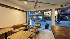Un restaurante con mesas y sillas de madera, piso de baldosas y vista a la calle.