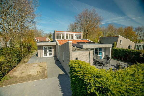 A modern house with a spacious patio, a covered outdoor area, and a well-maintained garden. - Holiday Home by Grevelingenmeer with Sauna (Brouwershaven)