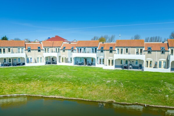 A row of townhouses with a grassy lawn and a small pond in the foreground.