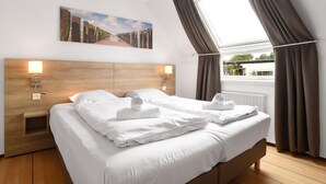 A hotel room with a large bed, two bedside tables, a headboard, a window with curtains, and a painting on the wall.