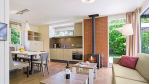 Ein modernes Wohnzimmer mit Kamin, einem Essbereich mit Tisch und Stühlen sowie einer Küche mit Backsteinwand und großen Fenstern.