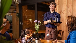 Ein Kellner serviert Gästen Getränke an einem Holztisch in einem Restaurant.