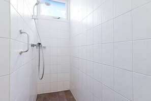 Een kleine douchekamer met witte tegels, een raam, een handdouche en een handdoucheslang.