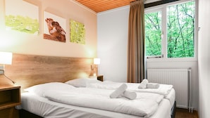 Ein Hotelzimmer mit zwei Betten, einem hölzernen Kopfteil, einem Fenster mit Blick auf Bäume und Bildern an der Wand.