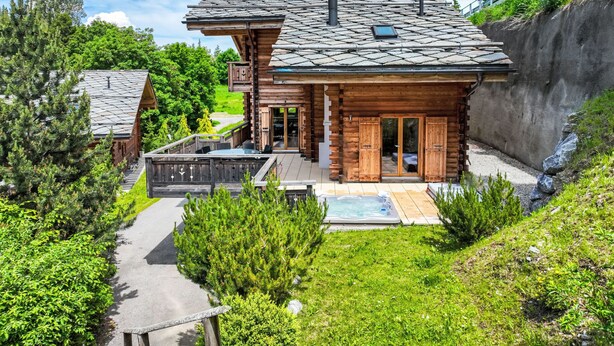 Una cabaña de madera con techo de piedra, un jacuzzi y una terraza.
