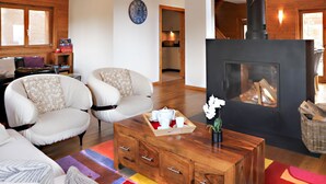 Una sala de estar acogedora con chimenea, dos sillones blancos, una mesa de centro de madera y un tapete colorido.