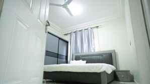 A bedroom with a bed, a ceiling fan, a window with curtains, and a door. - DAA DINGBE SUITES (Tamale)