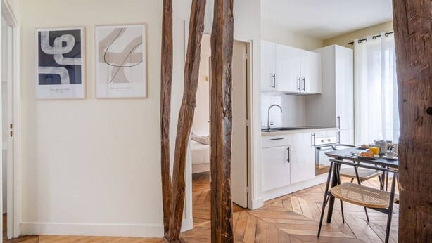 A modern kitchen with white cabinets, a dining area with a table and chairs, and two abstract art pieces on the wall.