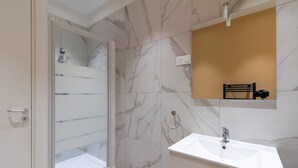 A modern bathroom with a glass shower enclosure, a white sink, and a marble-tiled wall.