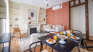 A modern dining area with a black table set for breakfast, a white sofa with patterned cushions, and a fireplace.