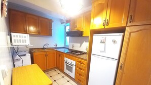 Een functionele keuken met houten kastjes, een ingebouwde oven, een koelkast en een kleine eettafel.