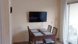Een eetgedeelte met een plafondventilator, een wandgemonteerde flatscreen-tv en een tafel met stoelen.
