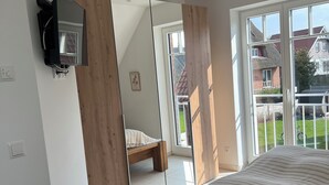 Un dormitorio con cama, televisor montado en la pared, un ventanal grande y un espejo que refleja la habitación.