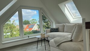 Un dormitorio tipo loft moderno con techo inclinado, ventanas amplias, un sofá acogedor y una mesita pequeña.