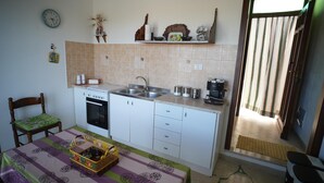 A compact kitchen with white cabinets, a stove, a sink, and a coffee maker. - The House of Flowers, in the heart of the Gulf of Macari 2.5 km from the sea. (Castelluzzo)