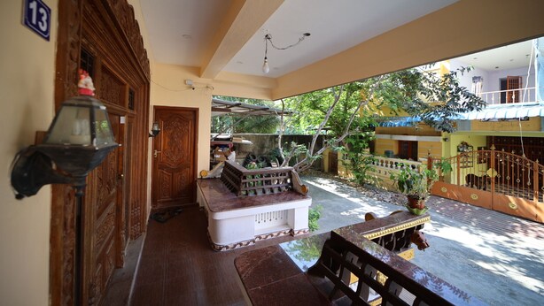 A spacious corridor with a wooden door, a bench, and a small table with a potted plant. - LE PONDY HOMESTAY (Puducherry)