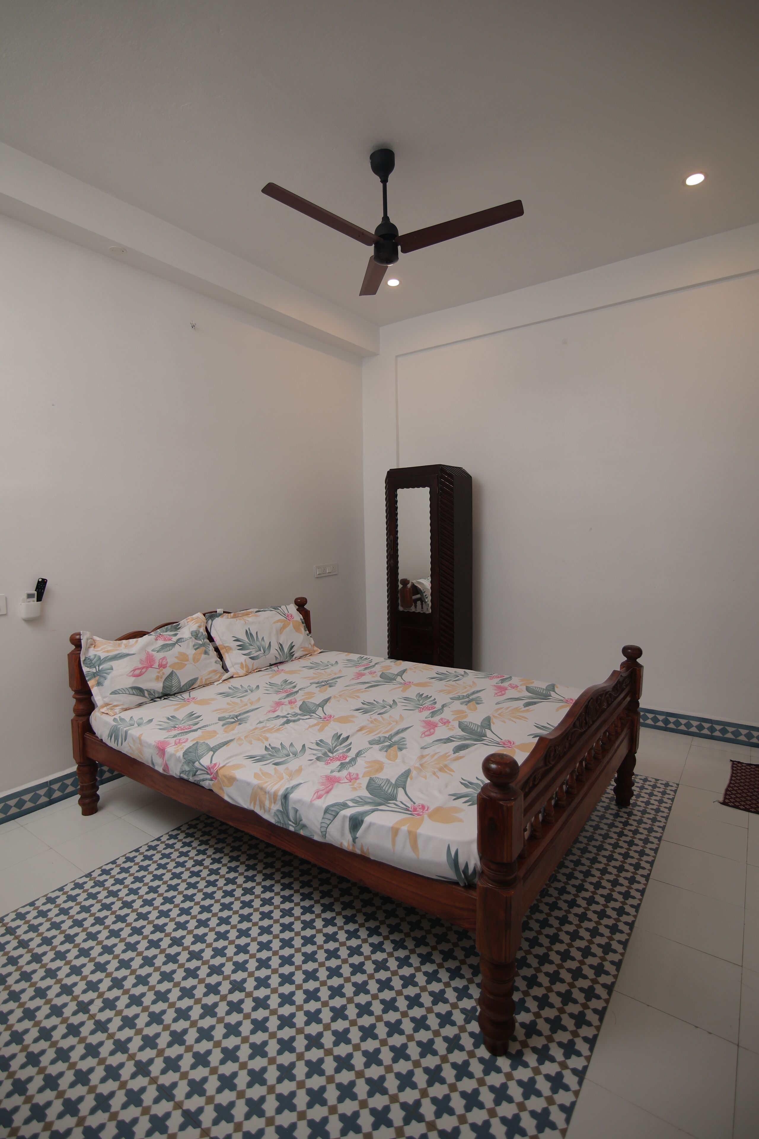 Une chambre à coucher avec un lit en bois, un ventilateur de plafond, un miroir et des carreaux de sol à motifs.