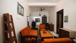 A dining area with a long table, orange upholstered chairs, and a ceiling fan. - LE PONDY HOMESTAY (Puducherry)