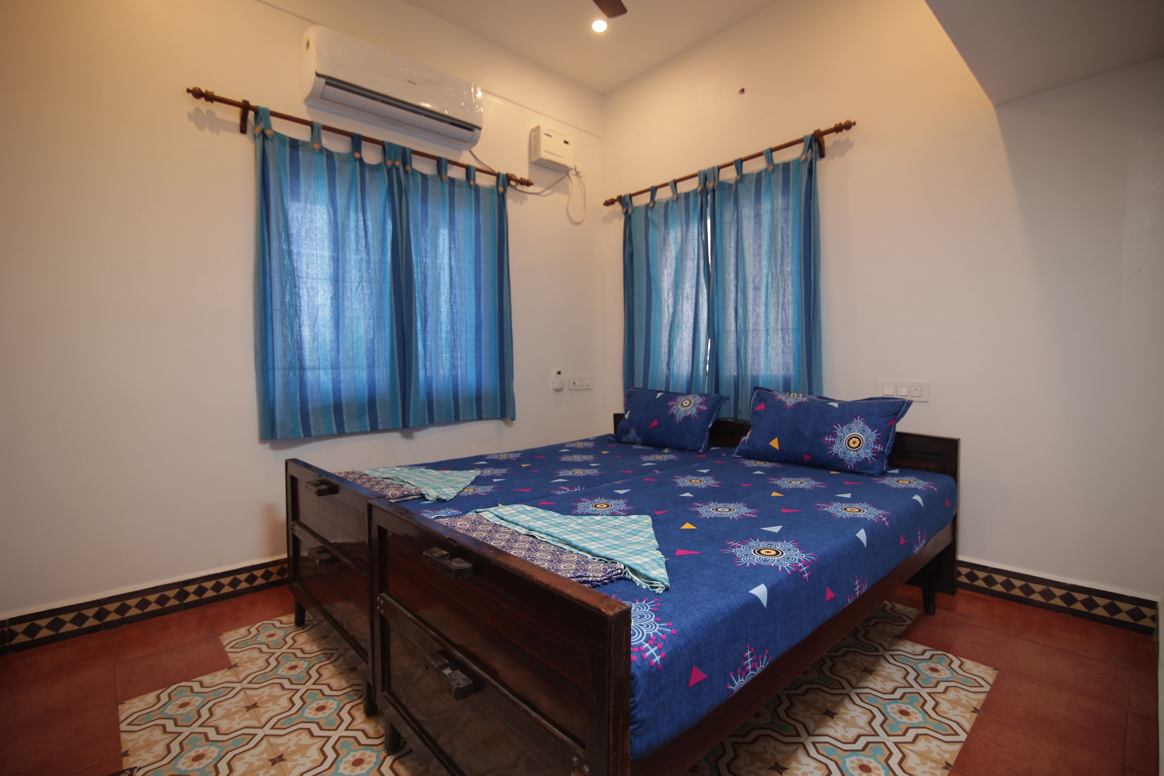 A bedroom with a bed, curtains, an air conditioning unit, and patterned floor tiles.