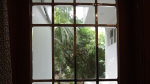 A window with a grid pattern, allowing a view of greenery outside. - LE PONDY HOMESTAY (Puducherry)