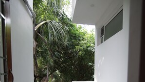 A narrow hallway with a tiled floor, a white wall, and a window overlooking a lush green area. - LE PONDY HOMESTAY (Puducherry)