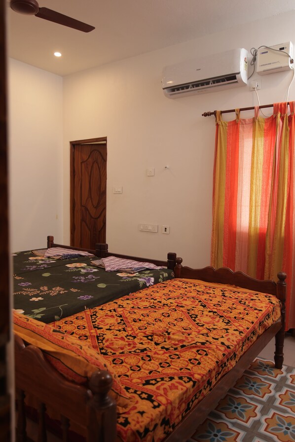 A room with two beds, an air conditioning unit, a ceiling fan, a wooden door, and a curtain.