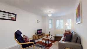 Una sala de estar con sofá, sillón, mesa de centro y un televisor que muestra 'NETFLIX'.
