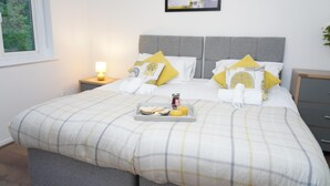 A neatly made bed with a plaid bedspread, two pillows, a tray with breakfast items, and a bedside lamp. - 4guests-parking-2br-familyfriendly (London)
