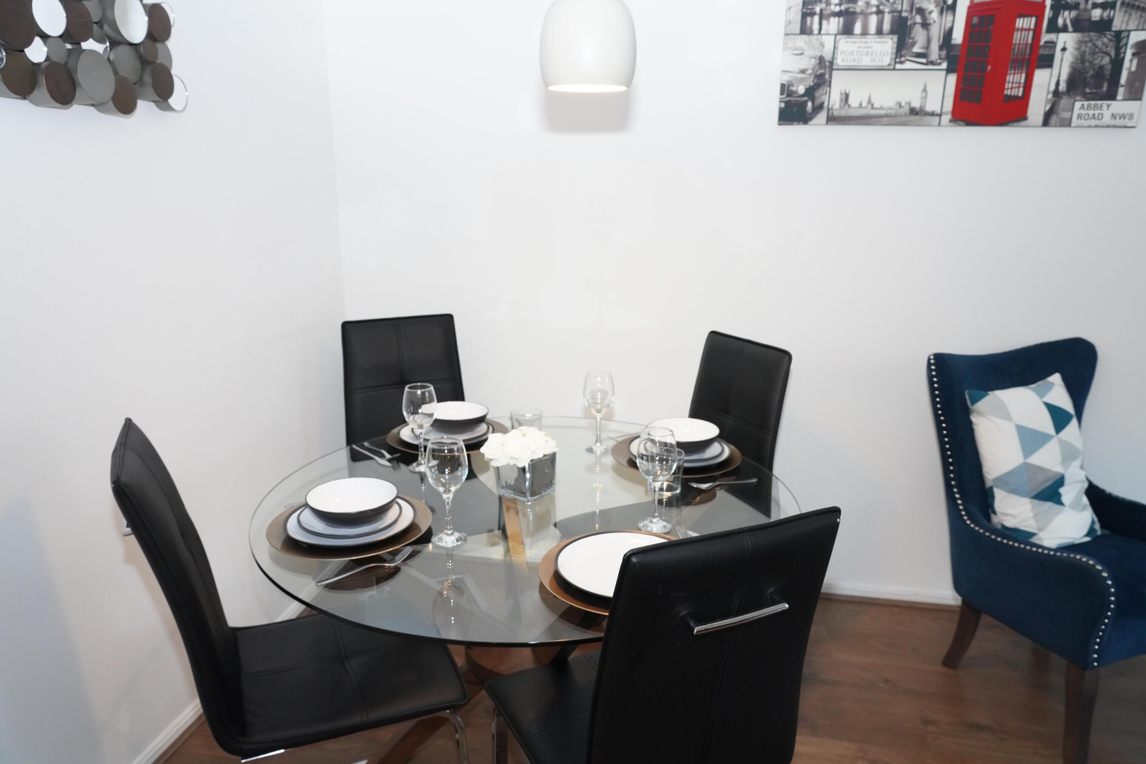 A dining area with a round glass table, black chairs, and a blue chair with a patterned cushion.